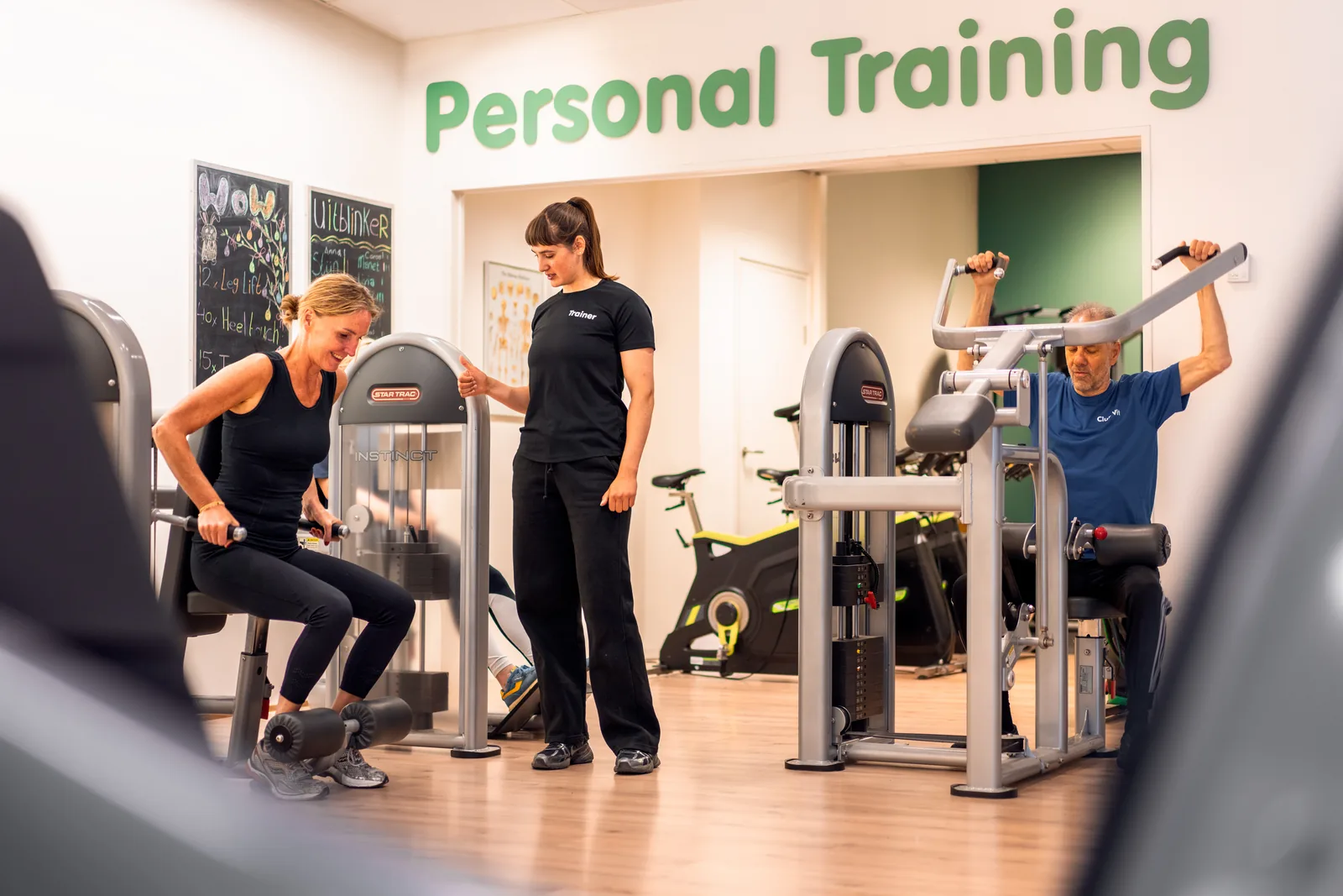 Personal trainer begeleidt twee leden in de personal-trainingruimte van Club Vit